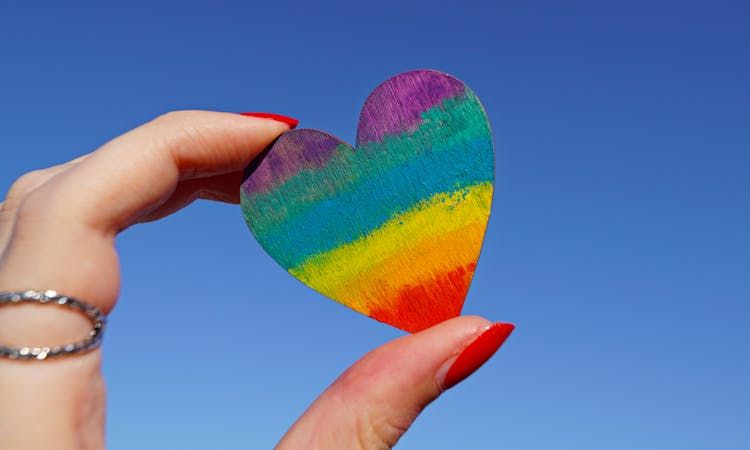 pessoa segura um coração com as cores da bandeira LGBTQIAPN+